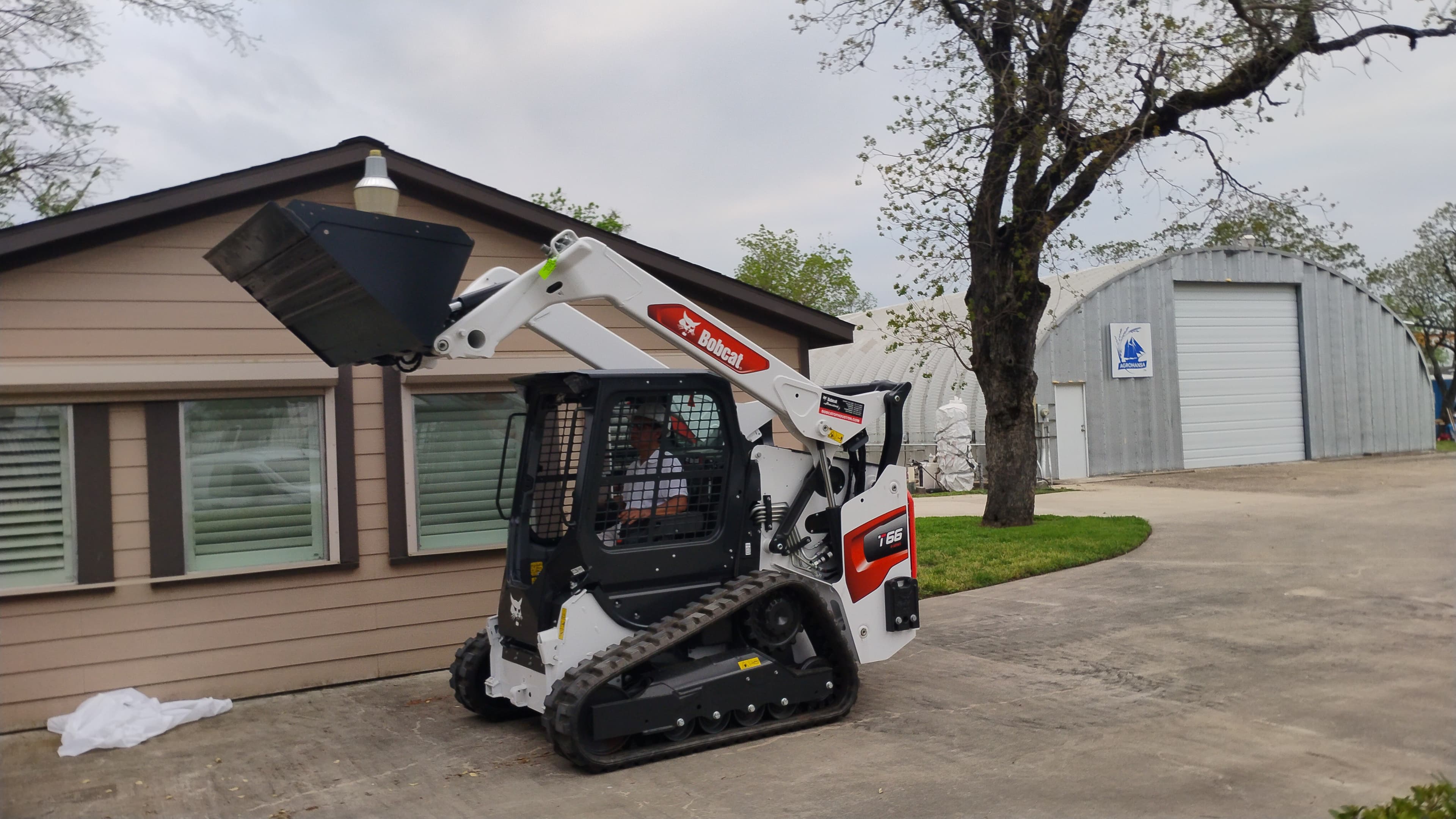 Bobcat T66 compact track loader in Houston with the loader arms raised near a building.